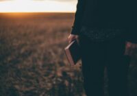 person holding book while standing on field