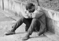 man in gray jacket and black pants sitting on concrete bench