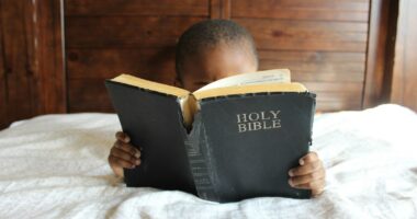 boy reading Holy Bible while lying on bed